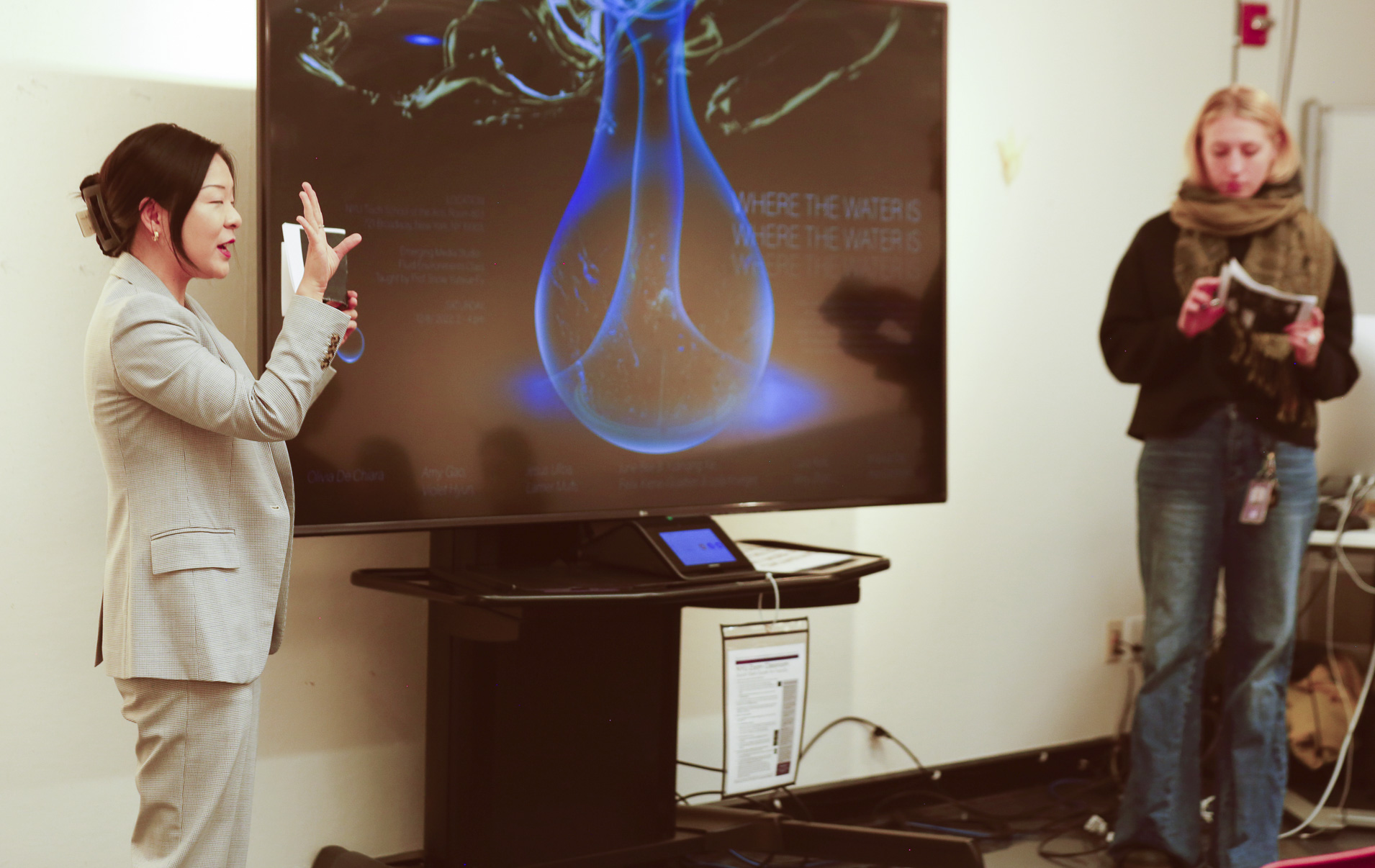 Professor Snow Fu and student Cora Rafe both stand near a large television